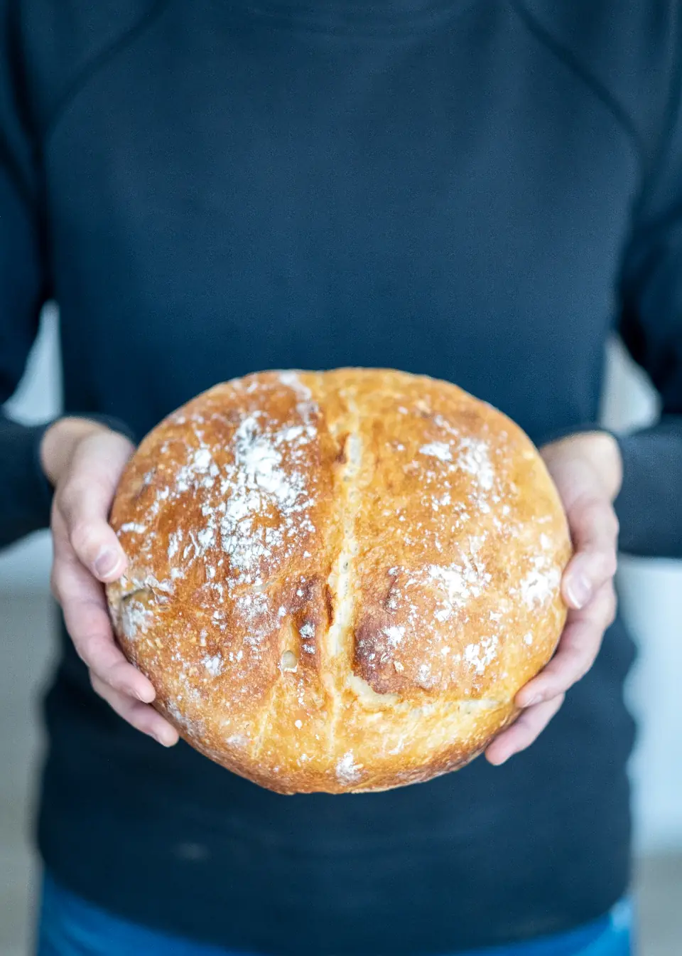 Zwei Hände halten ein frisch gebackenes, bemehltes Brot